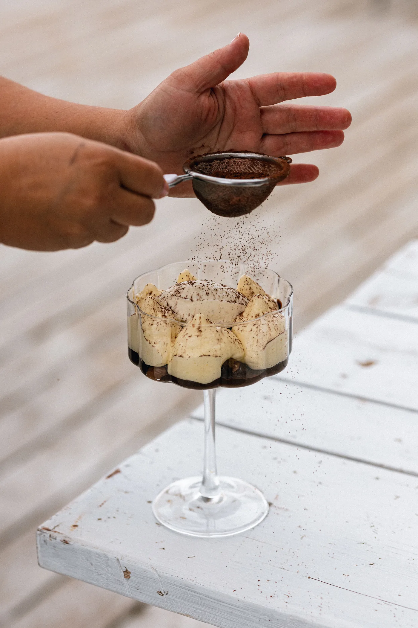 Eine Hand staubt Kakao über einem Dessert in einem Glas